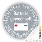 Prüfaufkleber, Prüfplakette rund, Farbe- Grau, Text "Batterie gewechselt" in Weiss. Icon Batterie, Startjahr- 25, Monatszahlen Oben und Jahreszahlen Unten in Kreisform.