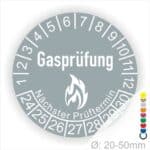 Prüfplaketten, Prüfetiketten rund, Farbe- Grau, Text "Gasprüfung" in Weiß danach eine Flamme als Pictogramm oder Icon in Weiß, Startjahr- 24, Monatszahlen Oben und Jahreszahlen Unten in Kreisform. Über den Jahreszahlen Text "Nächster Prüftermin"