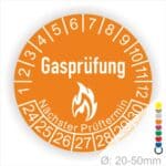 Prüfplaketten, Prüfetiketten rund, Farbe- Orange, Text "Gasprüfung" in Weiß danach eine Flamme als Pictogramm oder Icon in Weiß, Startjahr- 24, Monatszahlen Oben und Jahreszahlen Unten in Kreisform. Über den Jahreszahlen Text "Nächster Prüftermin"