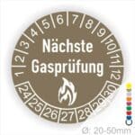 Prüfplaketten rund, Farbe- Braun, Text "Nächste Gasprüfung" in Weiß danach eine Flamme als Pictogramm oder Icon in Weiß, Startjahr- 24, Monatszahlen Oben und Jahreszahlen Unten in Kreisform.