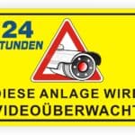 Schild mit der Aufschrift "24 Stunden - Diese Anlage wird videoüberwacht" und einem Symbol einer Überwachungskamera auf gelbem Hintergrund.