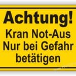 Hinweisschild mit der Aufschrift "Achtung! Kran Not-Aus Nur bei Gefahr betätigen" in gelber Farbe.