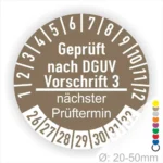 Alt-Text: Runde Prüfplakette mit der Aufschrift "Geprüft nach DGUV Vorschrift 3", die den nächsten Prüftermin anzeigt. Die Plakette hat eine Durchmesserangabe von 20-50mm und zeigt die Zahlen 1 bis 12 sowie 26 bis 32 zur Kennzeichnung von Prüfterminen.