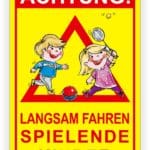 Achtungsschild mit der Aufschrift "Langsam fahren, spielende Kinder" und Illustrationen von zwei spielenden Kindern, einem Jungen und einem Mädchen, die ein Ballspiel spielen.