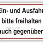 Schild mit der Aufschrift "Ein- und Ausfahrt bitte freihalten, auch gegenüber" zur Regelung des Verkehrsflusses und zur Gewährleistung der Sicherheit in einem Parkplatzbereich.