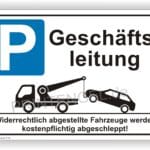 Schild mit der Aufschrift "Geschäftsleitung" und einem Piktogramm eines Abschleppwagens, das ein falsch geparktes Auto hebt. Hinweis auf kostenpflichtiges Abschleppen von unrechtmäßig abgestellten Fahrzeugen.