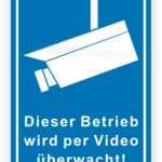 Schild mit der Aufschrift "Dieser Betrieb wird per Video überwacht!" und einem Bild einer Überwachungskamera, das auf die Videoüberwachung in einem Geschäft hinweist.