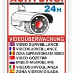 Schild zur Videoüberwachung mit einer Überwachungskamera, das auf 24-Stunden-Überwachung hinweist. Mehrsprachige Hinweise auf Videoüberwachung in Englisch, Französisch, Rumänisch, Türkisch, Russisch, Italienisch, Spanisch und Arabisch.