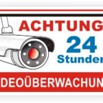 Schild mit der Aufschrift "Achtung 24 Stunden Videoüberwachung" und einer Abbildung einer Überwachungskamera, das auf permanente Sicherheitsüberwachung hinweist.