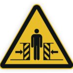 Warnschild mit einer Person zwischen zwei beweglichen Barrieren, das auf Gefahren hinweist.