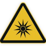 Warnschild für Sonnenstrahlung, gelbes Dreieck mit schwarzem Symbol einer Sonne.