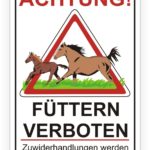 Achtungsschild mit der Aufschrift "Füttern verboten" und Bildern von zwei laufenden Pferden, das vor möglichen rechtlichen Konsequenzen bei Verstößen warnt.
