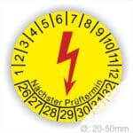 E-Check Prüfplaketten rund, Farbe- Gelb, ein Elektro- Pfeil in Rot, Startjahr- 26, Monatszahlen Oben und Jahreszahlen Unten in Kreisform. Über den Jahreszahlen Text "Nächster Prüftermin"