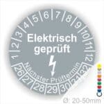 Prüfplaketten rund Farbe- Grau, Text "Elektrisch geprüft" in Weiß Startjahr- 26 mit Elektro Pfeil, Monatszahlen Oben und Jahreszahlen Unten in Kreisform