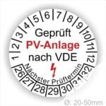 Prüfplaketten rund, Farbe- Weß, Text "Geprüft PV-Anlage nach VDE" in Schwarz danach ein Elektro- Pfeil in Rot, Startjahr- 26, Monatszahlen Oben und Jahreszahlen Unten in Kreisform. Über den Jahreszahlen Text "Nächster Prüftermin"