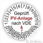 Prüfplaketten rund, Farbe- Weß, Text "Geprüft PV-Anlage nach VDE" in Schwarz danach ein Elektro- Pfeil in Rot, Startjahr- 27, Monatszahlen Oben und Jahreszahlen Unten in Kreisform. Über den Jahreszahlen Text "Nächster Prüftermin"