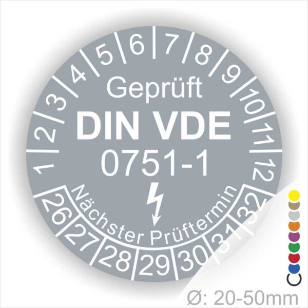 Prüfplaketten rund, Farbe- Grau, Text "Geprüft gemäß DIN VDE 0751-1" in Weiß danach ein Elektro- Pfeil in Weiß, Startjahr- 26, Monatszahlen Oben und Jahreszahlen Unten in Kreisform. Über den Jahreszahlen Text "Nächster Prüftermin"