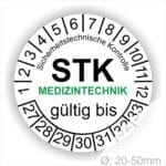 Prüfetiketten rund, Farbe- Weiß, Text "Sicherheitstechnische Kontrolle, STK MEDIZINTECHNIK gültig bis" in Schwarz. Startjahr- 27, Monatszahlen Oben und Jahreszahlen Unten in Kreisform. über den Jahreszahlen Text.