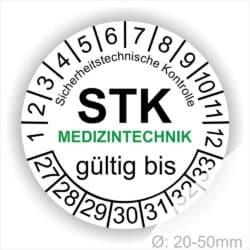 Prüfetiketten rund, Farbe- Weiß, Text "Sicherheitstechnische Kontrolle, STK MEDIZINTECHNIK gültig bis" in Schwarz. Startjahr- 27, Monatszahlen Oben und Jahreszahlen Unten in Kreisform. über den Jahreszahlen Text.