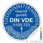 Prüfplakette, Prüfetikette rund, Farbe- Blau, Text "Geprüft gemäß VDE 0100-0723" in Weiß danach ein Elektro- Pfeil in Weiß, Startjahr- 26, Monatszahlen Oben und Jahreszahlen Unten in Kreisform. Über den Jahreszahlen Text "Nächster Prüftermin"