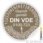 Prüfetiketten rund, Farbe- Braun, Text "Geprüft gemäß VDE 0100-0723" in Weiß danach ein Elektro- Pfeil in Weiß, Startjahr- 26, Monatszahlen Oben und Jahreszahlen Unten in Kreisform. Über den Jahreszahlen Text "Nächster Prüftermin"