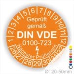 Prüfetiketten rund, Farbe- Orange, Text "Geprüft gemäß VDE 0100-0723" in Weiß danach ein Elektro- Pfeil in Weiß, Startjahr- 26, Monatszahlen Oben und Jahreszahlen Unten in Kreisform. Über den Jahreszahlen Text "Nächster Prüftermin"