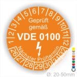 Prüfplaketten rund Farbe- Orange, Text "Geprüft gemäß VDE 0100" in Weiß danach ein Elektro- Pfeil in Weiß, Startjahr- 26, Monatszahlen Oben und Jahreszahlen Unten in Kreisform. Über den Jahreszahlen Text "Nächster Prüftermin"