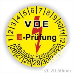 Prüfplaketten rund, Farbe- Gelb, Text "VDE E-Prüfung" in Schwarz in Hinergrund ein Elektro- Pfeil in Rot, Startjahr- 26, Monatszahlen Oben und Jahreszahlen Unten in Kreisform. Über den Jahreszahlen Text "Nächster Prüftermin"