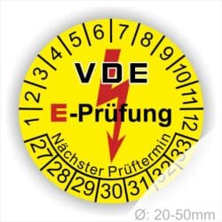 Prüfplaketten rund, Farbe- Gelb, Text "VDE E-Prüfung" in Schwarz in Hinergrund ein Elektro- Pfeil in Rot, Startjahr- 27, Monatszahlen Oben und Jahreszahlen Unten in Kreisform. Über den Jahreszahlen Text "Nächster Prüftermin"