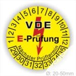 Prüfplaketten rund, Farbe- Gelb, Text "VDE E-Prüfung" in Schwarz in Hinergrund ein Elektro- Pfeil in Rot, Startjahr- 29, Monatszahlen Oben und Jahreszahlen Unten in Kreisform. Über den Jahreszahlen Text "Nächster Prüftermin"