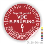 Rotes Prüfplakett mit der Aufschrift "Geprüft gemäß VDE E-Prüfung", das den nächsten Prüftermin anzeigt. Enthält eine Skala von 1 bis 12 und eine weitere von 27 bis 33. Durchmesser zwischen 20 und 50 mm.
