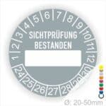 Prüfplakette, Prüfetikett rund, Farbe- Grau, Text "SICHTPRÜFUNG-BESTANDEN" in Weiß. Als nächstes kommt ein Beschriftungfeld / Leerfeld in Farbe Weiß. Startjahr- 24, Monatszahlen Oben und Jahreszahlen Unten in Kreisform.