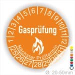 Prüfplaketten, Prüfetiketten rund, Farbe- Orange, Text "Gasprüfung" in Weiß danach eine Flamme als Pictogramm oder Icon in Weiß, Startjahr- 25, Monatszahlen Oben und Jahreszahlen Unten in Kreisform. Über den Jahreszahlen Text "Nächster Prüftermin"