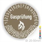 Prüfplaketten, Prüfetiketten rund, Farbe- Braun, Text "Gasprüfung" in Weiß danach eine Flamme als Pictogramm oder Icon in Weiß, Startjahr- 26, Monatszahlen Oben und Jahreszahlen Unten in Kreisform. Über den Jahreszahlen Text "Nächster Prüftermin"