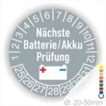 Prüfplaketten, Prüfetiketten rund, Farbe- Grau, Text "Nächste Batterie/Akku Prüfung" in Weiß. Icon Batterie, Startjahr- 25, Monatszahlen Oben und Jahreszahlen Unten in Kreisform.
