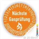 Prüfplaketten rund, Farbe- Orange, Text "Nächste Gasprüfung" in Weiß danach eine Flamme als Pictogramm oder Icon in Weiß, Startjahr- 25, Monatszahlen Oben und Jahreszahlen Unten in Kreisform.