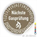 Prüfetiketten, Prüfplaketten rund, Farbe- Braun, Text "Nächste Gasprüfung" in Weiß danach eine Flamme als Pictogramm oder Icon in Weiß, Startjahr- 26, Monatszahlen Oben und Jahreszahlen Unten in Kreisform.