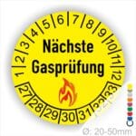 Prüfplaketten, Prüfetiketten rund, Farbe- Gelb, Text "Nächste Gasprüfung" in Schwarz danach eine Flamme als Pictogramm oder Icon in Rot, Startjahr- 27, Monatszahlen Oben und Jahreszahlen Unten in Kreisform. Über den Jahreszahlen.