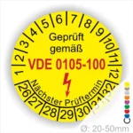 Gelbes Prüfplakett mit der Aufschrift "Geprüft gemäß VDE 0105-100" und Angaben zum nächsten Prüftermin sowie Durchmesser von 20-50 mm.