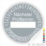 Prüfplakette, Wartungsplakette rund, Farbe- Grau, Text "Nächster Prüftermin" in Weiß. Als nächstes kommt ein Beschriftung Feld / Leer Feld in Farbe Weiß. Startjahr- 27, Monatszahlen Oben und Jahreszahlen Unten in Kreisform.