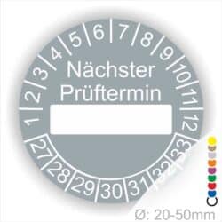 Prüfplakette, Wartungsplakette rund, Farbe- Grau, Text "Nächster Prüftermin" in Weiß. Als nächstes kommt ein Beschriftung Feld / Leer Feld in Farbe Weiß. Startjahr- 27, Monatszahlen Oben und Jahreszahlen Unten in Kreisform.