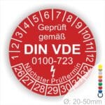 Prüfetiketten rund, Farbe- Rot, Text "Geprüft gemäß VDE 0100-0723" in Weiß danach ein Elektro- Pfeil in Weiß, Startjahr- 26, Monatszahlen Oben und Jahreszahlen Unten in Kreisform. Über den Jahreszahlen Text "Nächster Prüftermin"