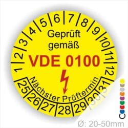Prüfplaketten rund Farbe- Gelb, Text "Geprüft gemäß VDE 0100" in Schwarz danach ein Elektro- Pfeil in Rot, Startjahr- 25, Monatszahlen Oben und Jahreszahlen Unten in Kreisform. Über den Jahreszahlen Text "Nächster Prüftermin"