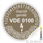 Prüfplaketten rund Farbe- Braun, Text "Geprüft gemäß VDE 0100" in Weiß danach ein Elektro- Pfeil in Weiß, Startjahr- 26, Monatszahlen Oben und Jahreszahlen Unten in Kreisform. Über den Jahreszahlen Text "Nächster Prüftermin"