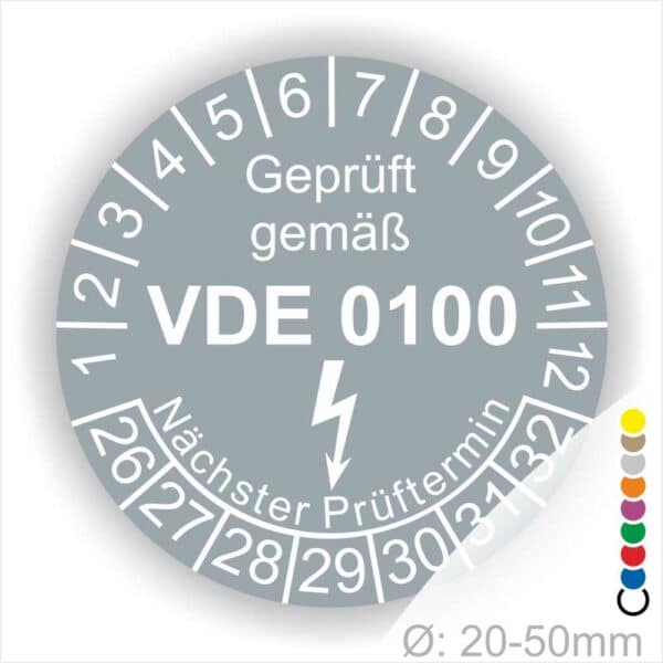 Prüfplaketten rund Farbe- Grau, Text "Geprüft gemäß VDE 0100" in Weiß danach ein Elektro- Pfeil in Weiß, Startjahr- 26, Monatszahlen Oben und Jahreszahlen Unten in Kreisform. Über den Jahreszahlen Text "Nächster Prüftermin"