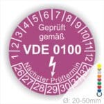 Prüfplaketten rund Farbe- Lila, Text "Geprüft gemäß VDE 0100" in Weiß danach ein Elektro- Pfeil in Weiß, Startjahr- 26, Monatszahlen Oben und Jahreszahlen Unten in Kreisform. Über den Jahreszahlen Text "Nächster Prüftermin"