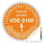Prüfplaketten rund Farbe- Orange, Text "Geprüft gemäß VDE 0100" in Weiß danach ein Elektro- Pfeil in Weiß, Startjahr- 26, Monatszahlen Oben und Jahreszahlen Unten in Kreisform. Über den Jahreszahlen Text "Nächster Prüftermin"