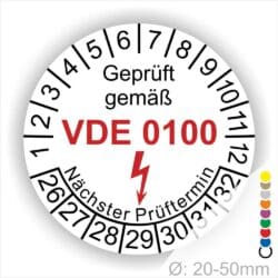 Prüfplaketten rund Farbe- Weiß, Text "Geprüft gemäß VDE 0100" in Schwarz danach ein Elektro- Pfeil in Rot, Startjahr- 26, Monatszahlen Oben und Jahreszahlen Unten in Kreisform. Über den Jahreszahlen Text "Nächster Prüftermin"