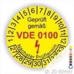Prüfaufkleber rund, Farbe- Gelb, Text "Geprüft gemäß VDE 0100" in Schwarz danach ein Elektro- Pfeil in Rot, Startjahr- 27, Monatszahlen Oben und Jahreszahlen Unten in Kreisform. Über den Jahreszahlen Text "Nächster Prüftermin"