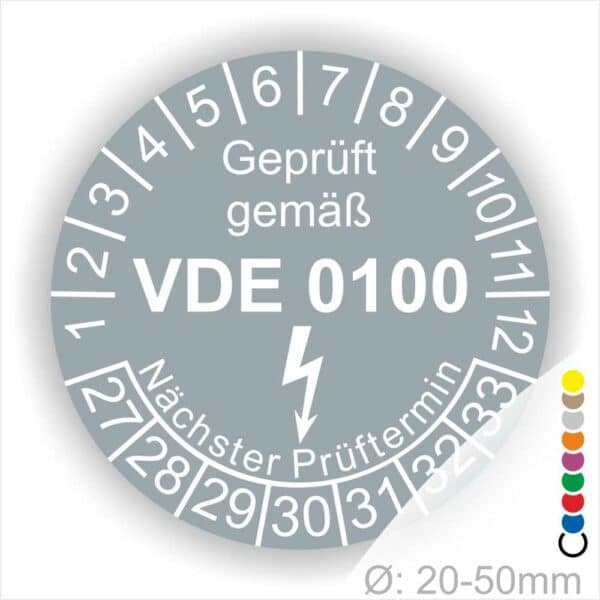 Prüfaukleber rund Farbe- Grau, Text "Geprüft gemäß VDE 0100" in Weiß danach ein Elektro- Pfeil in Weiß, Startjahr- 27, Monatszahlen Oben und Jahreszahlen Unten in Kreisform. Über den Jahreszahlen Text "Nächster Prüftermin"
